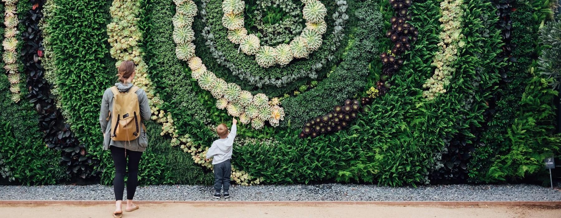 mother and child standing in front of a mural made of plants